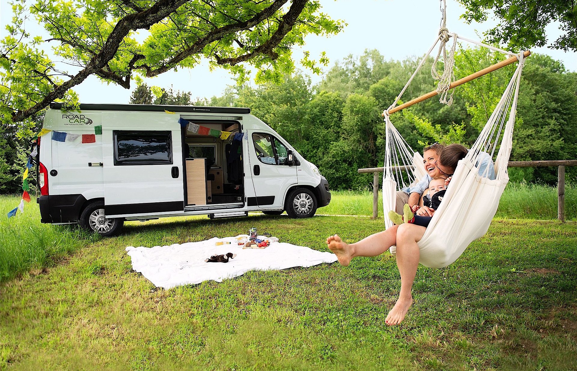 Roadcar bietet praktische und komfortable Kompaktcamper. Ein Paar turtelt auf einer Hängematte vor einem Kompaktcamper herum.