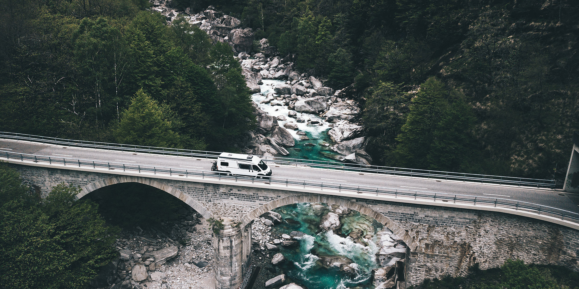 Ein Camper-Van fährt über eine altertümliche Brücke.