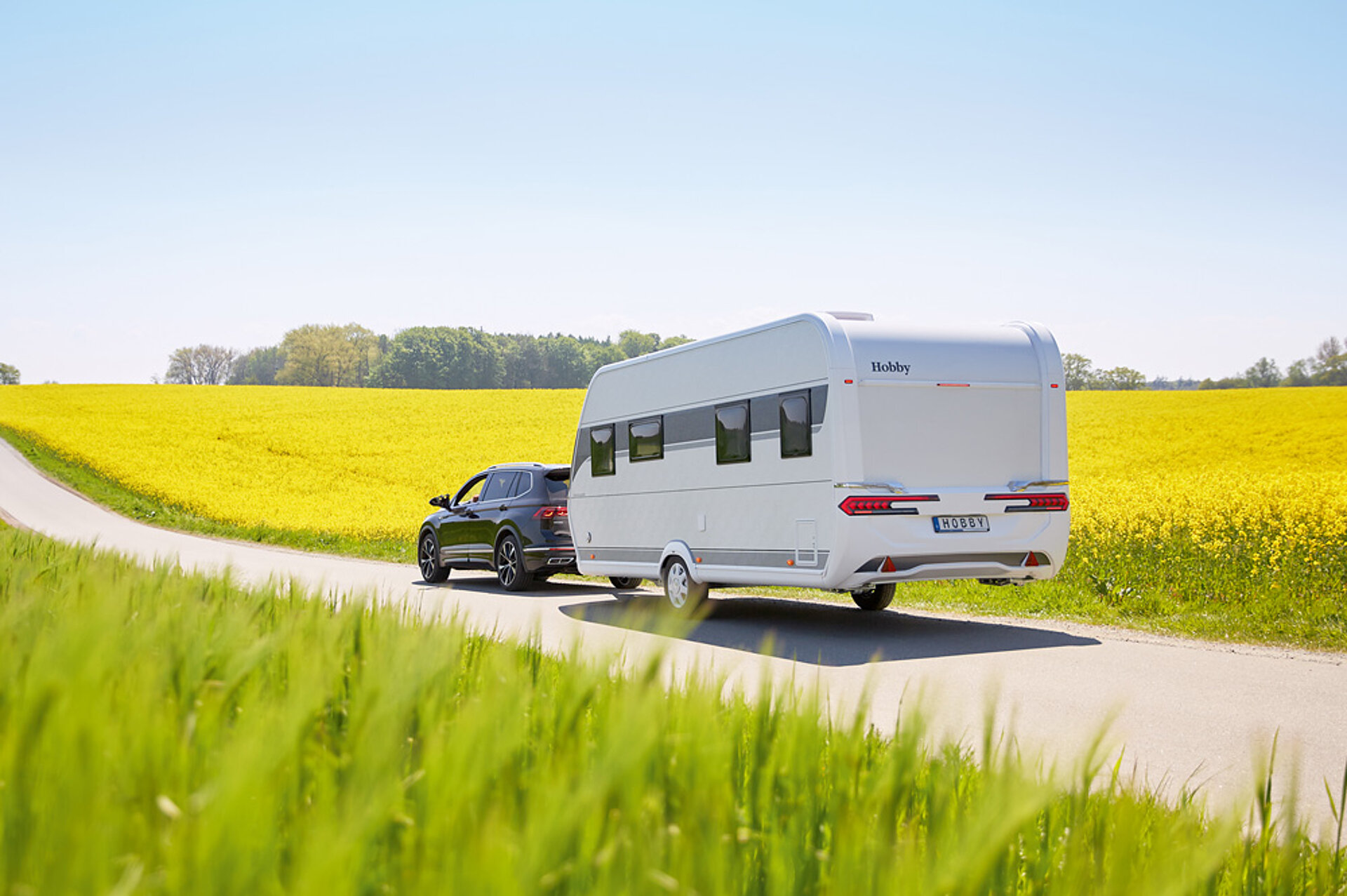 Ein exzellentes Preis-Leistungs-Verhältnis und viel Auswahl – das ist Hobby! Ein Hobby Wohnwagen wird von einem PKW eine Straße entlang gezogen.