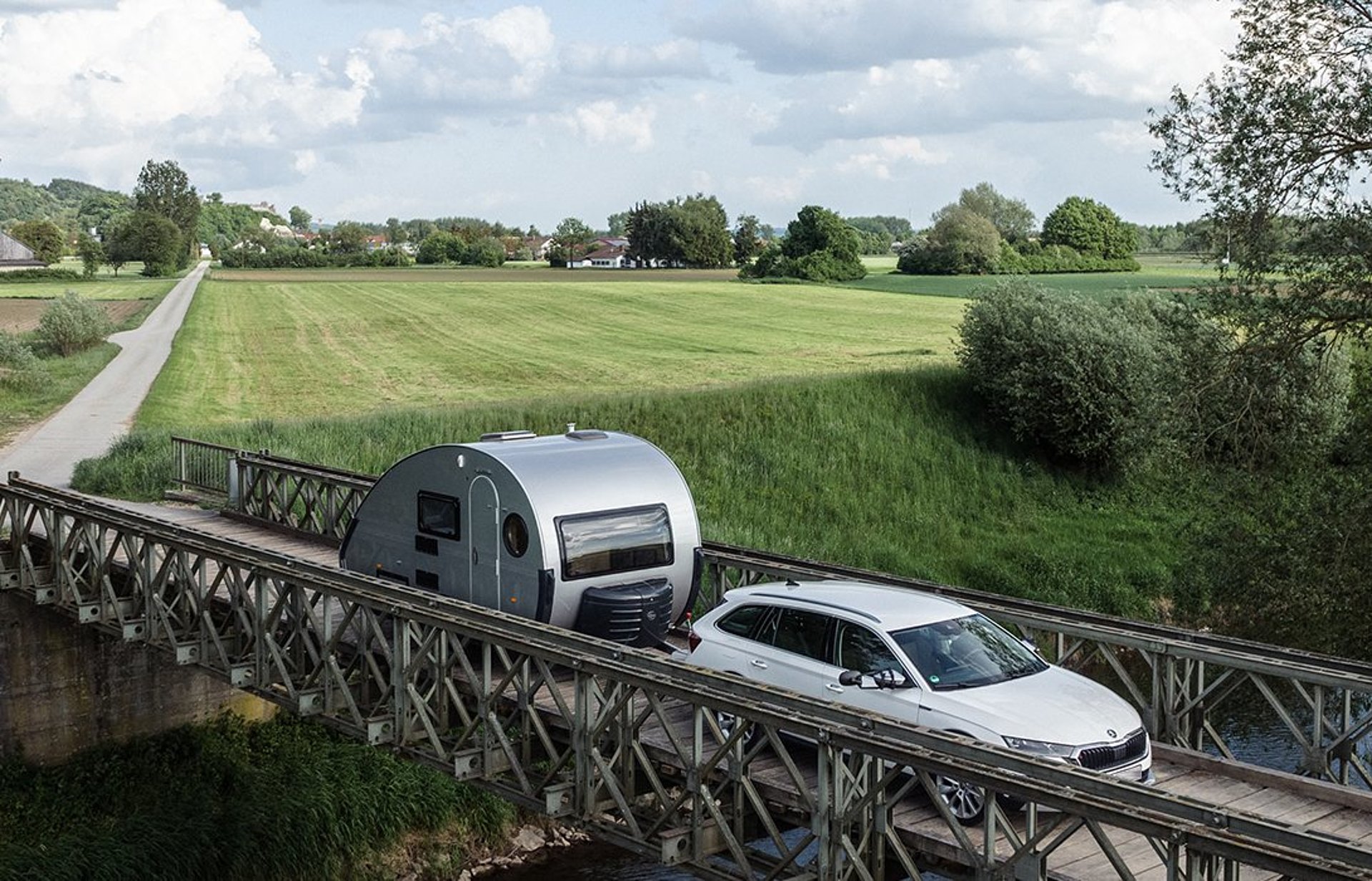 Wohnwagen von T@B begeistern mit einem kultigen Retro-Look. Ein Auto zieht einen kleinen Wohnwagen von T@B über eine Brücke.