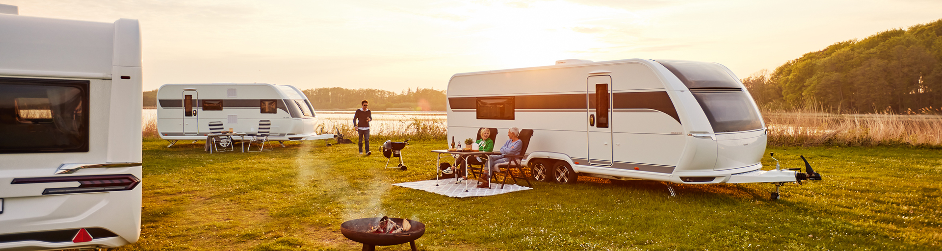 Mehrere Familien campen mit Hobby Wohnwagen an einem See.